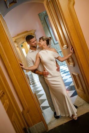 Elegant couple in white attire sharing a romantic moment in a golden doorway of a grand building.