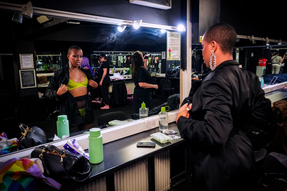 Performers prepare backstage in a dressing room with mirrors and lights before a show.
