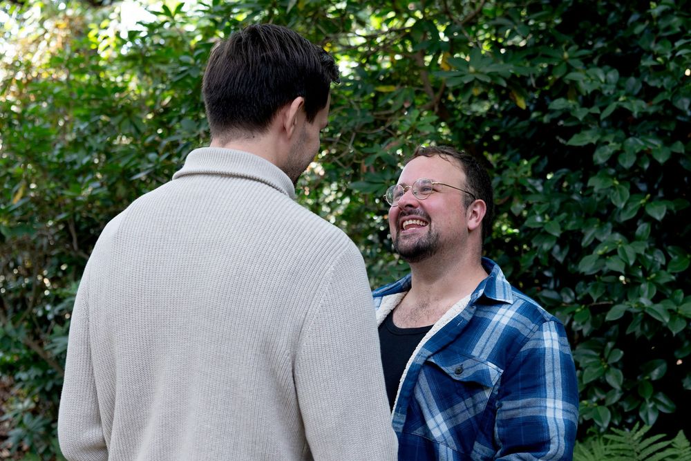 Two men having a conversation outdoors surrounded by lush green trees and shrubs.
