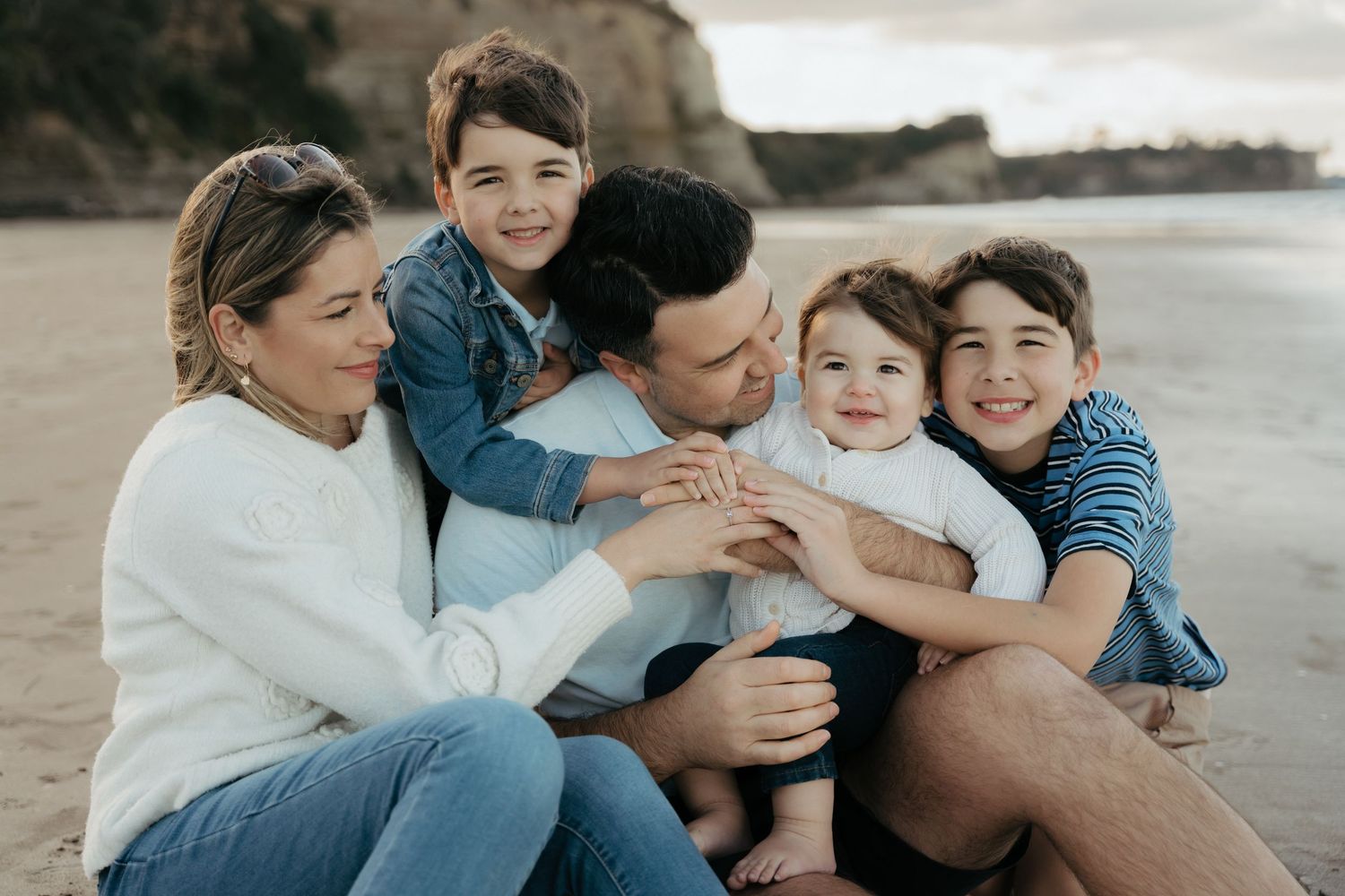 Happy family of five sharing a joyful moment together on a sandy beach, with cliffs in the background.