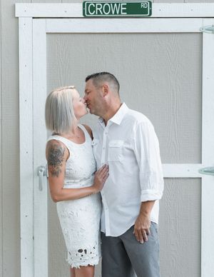 Couple kissing in white outfits near a Crowe Road street sign, woman with tattoo sleeve, outdoor engagement photo.