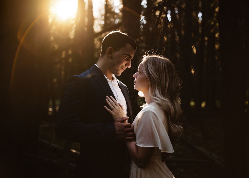 Intimate golden hour portrait of a couple in a backlit forest, by a Calgary wedding photographer