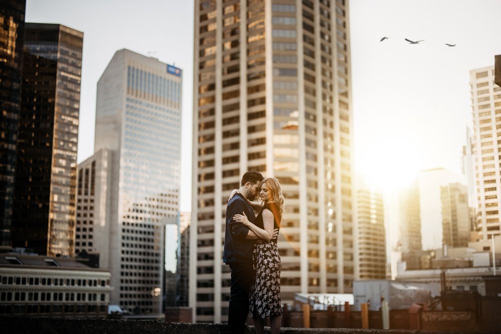 Couple embracing among downtown Calgary skyscrapers at golden sunset, by a Calgary wedding photographer