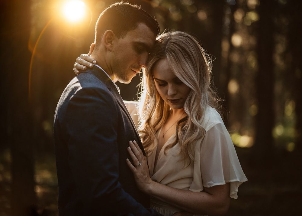 Bride and groom resting forehead to forehead in warm golden forest light, by a Calgary wedding photographer