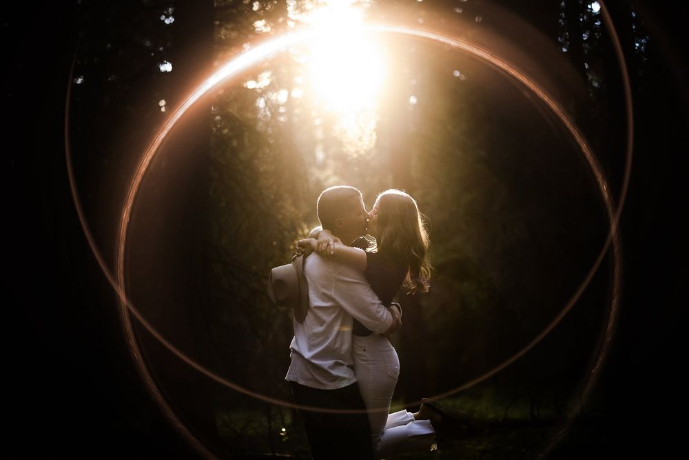 Couple embracing in a dark forest framed by a glowing ring of light, by a Calgary wedding photographer
