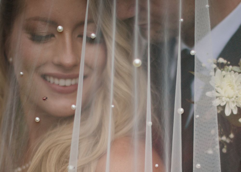 Close-up of a smiling bride seen through her pearl-studded veil, by a Calgary wedding photographer