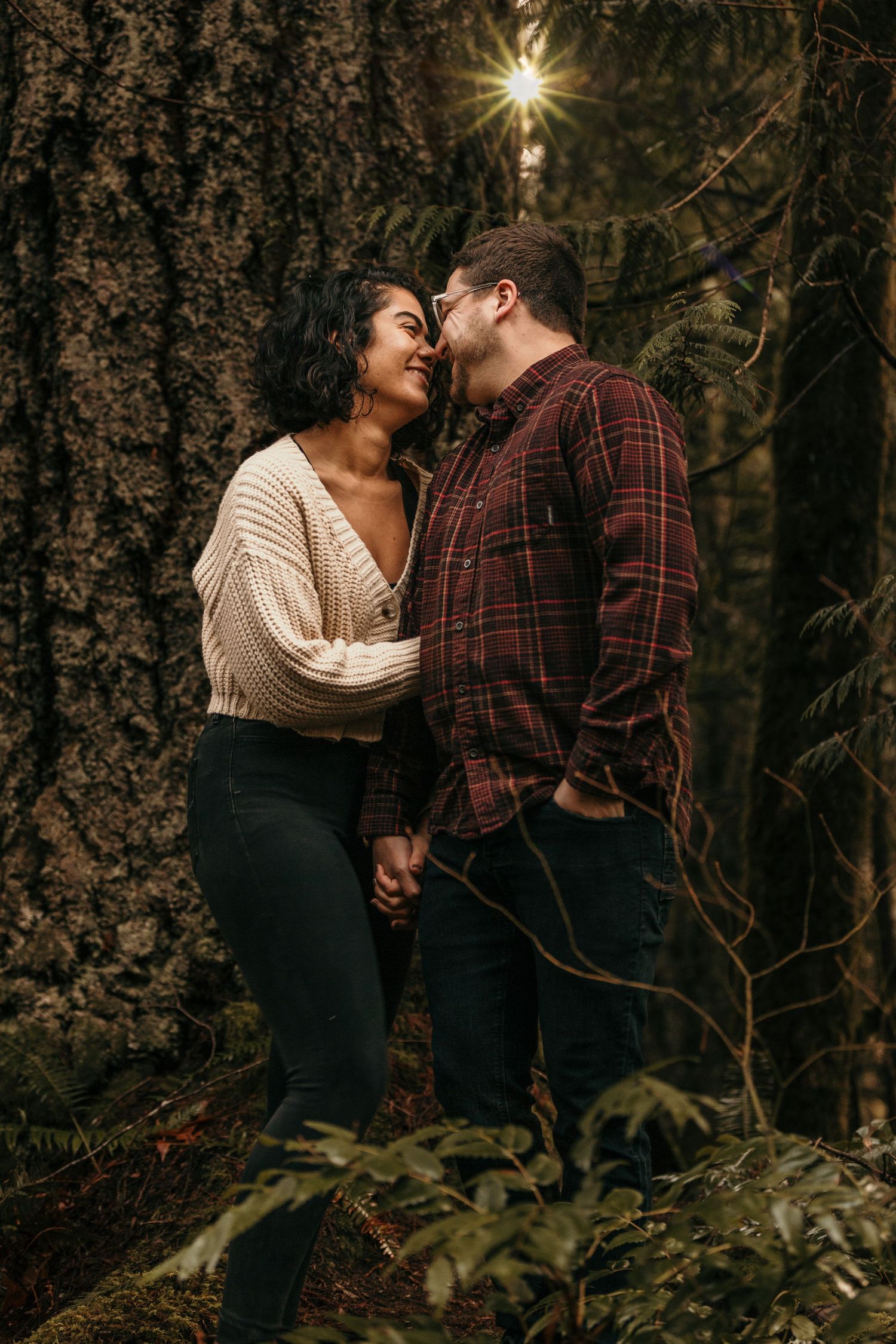 Couple sharing a romantic moment in a lush forest, holding hands and smiling at each other near a large tree in the Hoh Rainforest
