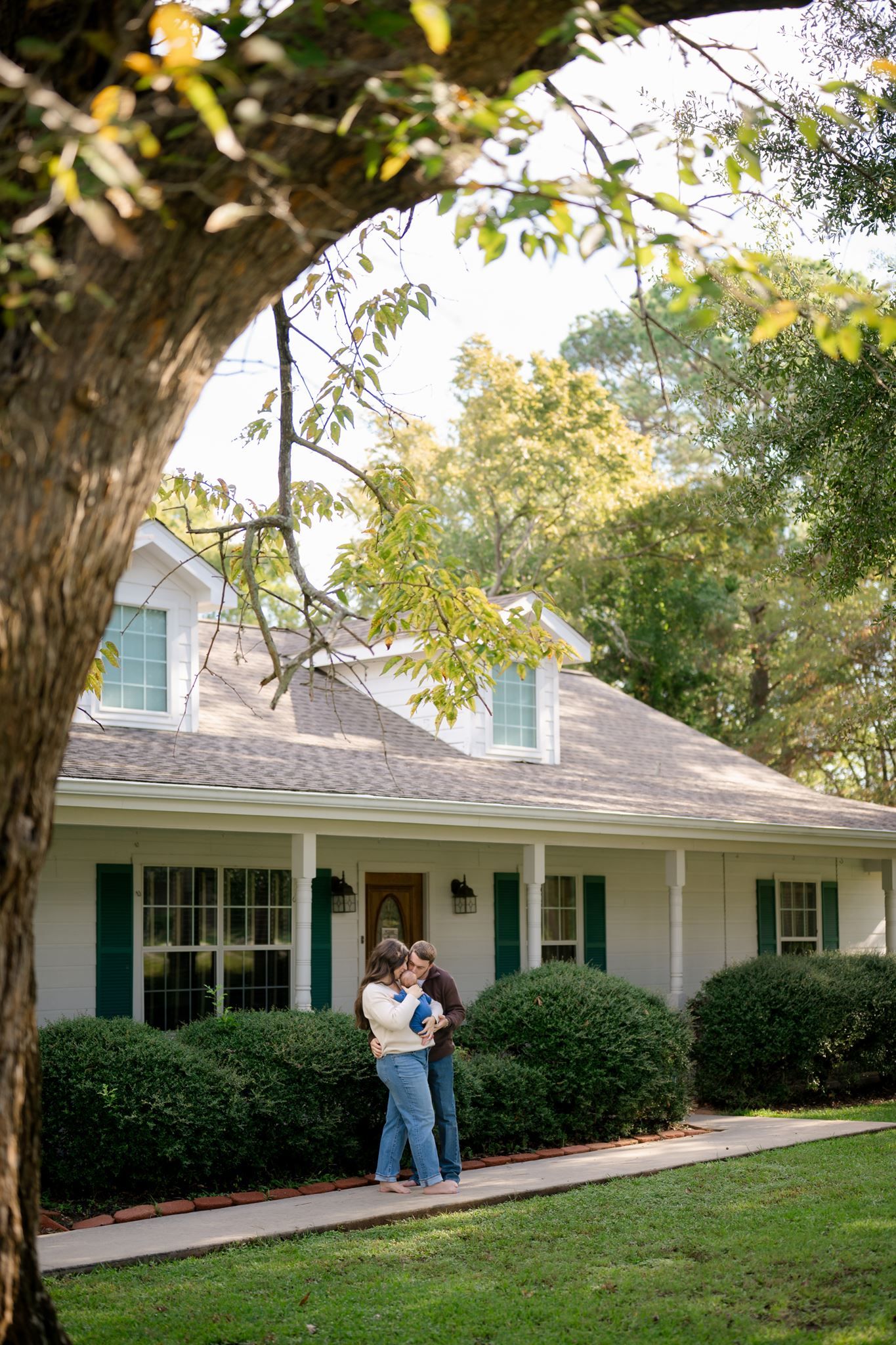 Parents with their newborn standing in front of their ranch style home in Willis, Texas.