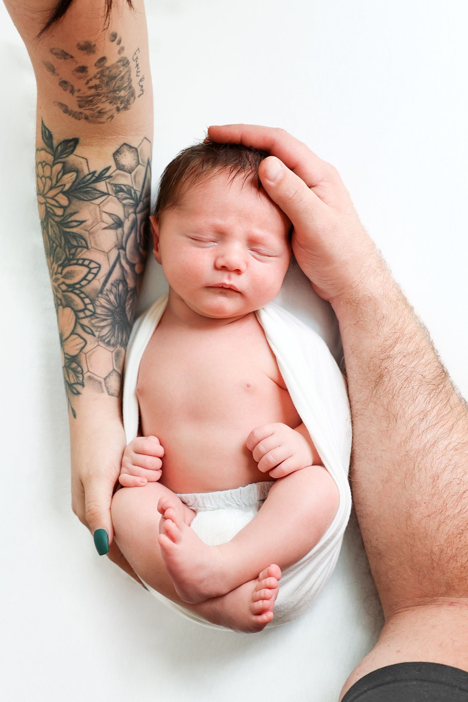 Newborn baby sleeping peacefully cradled in parents hands, one arm with floral tattoo.