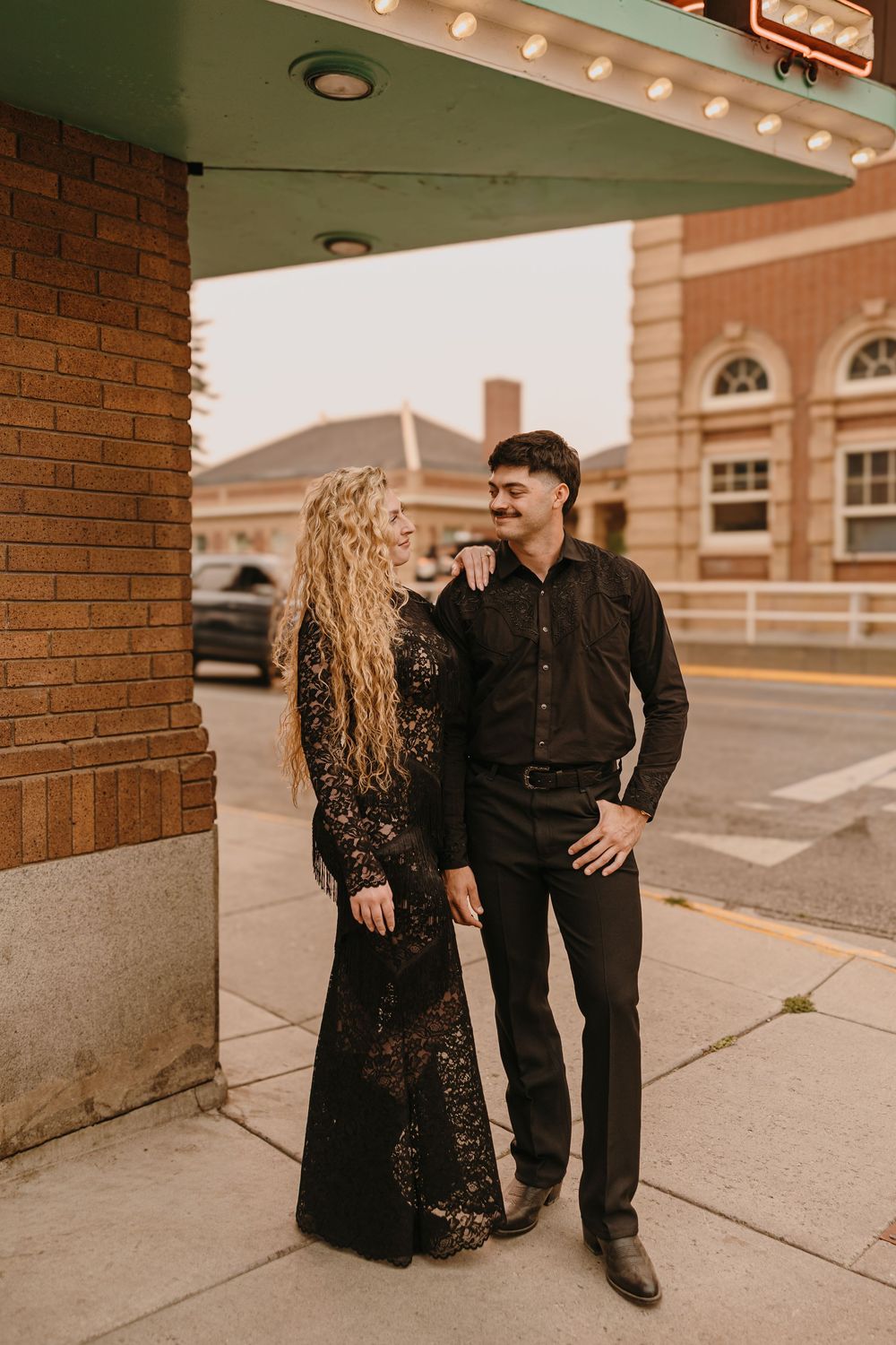 Couple poses under the Murray Hotel Neon light signs in Livingston, Montana for their welcome party pre-wedding - Welcome Party Photographer
