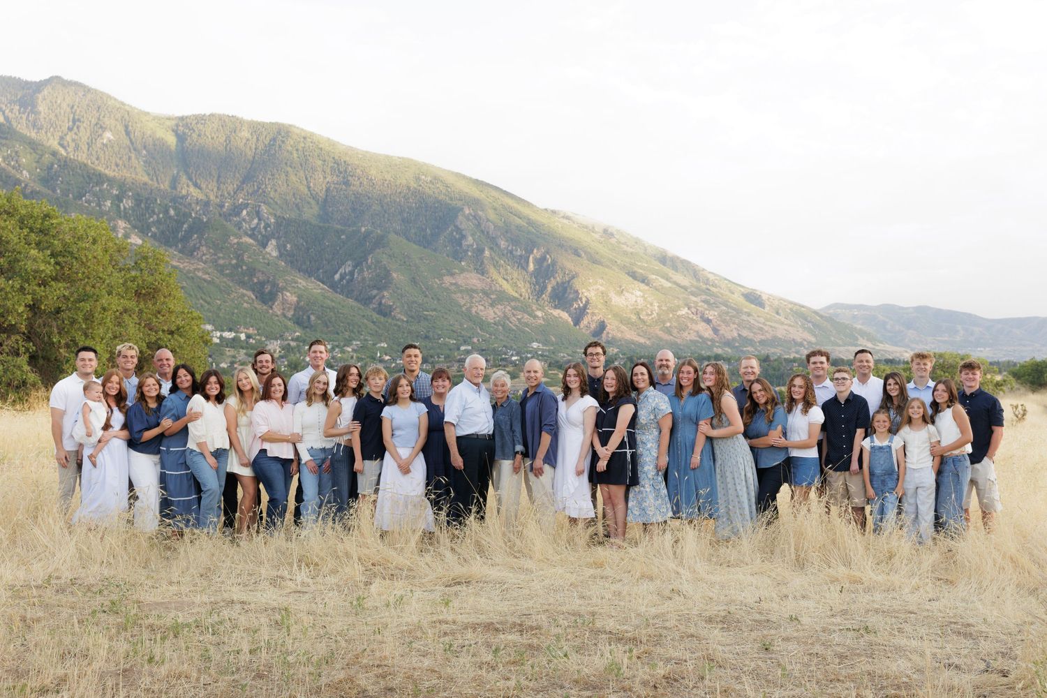 Large multigenerational family group photo in dry golden meadow with dramatic mountain range in background.