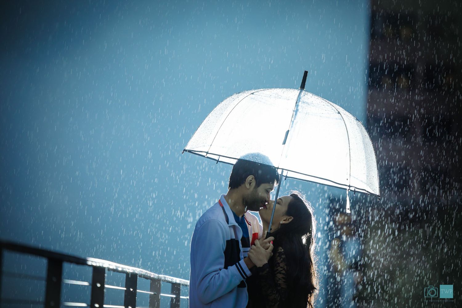A couple shares a romantic kiss under a clear umbrella in heavy rain- by our Memphis wedding photography and videography team