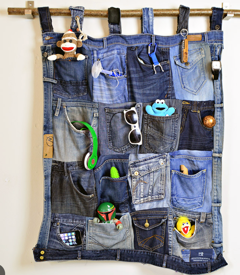 Upcycled denim jeans pockets wall organizer hanging on a stick, storing toys, sunglasses, and small items.