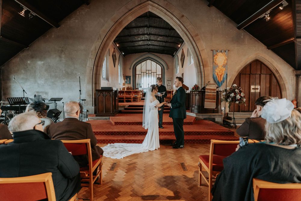 Bride and groom exchanging vows at altar in traditional English stone church.