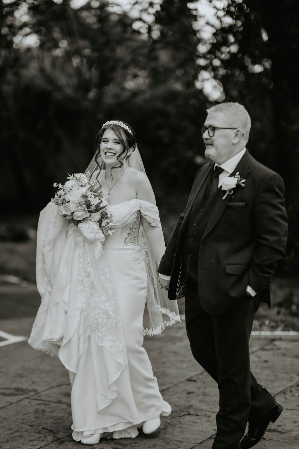 Black and white photo of smiling bride and father walking together before ceremony.