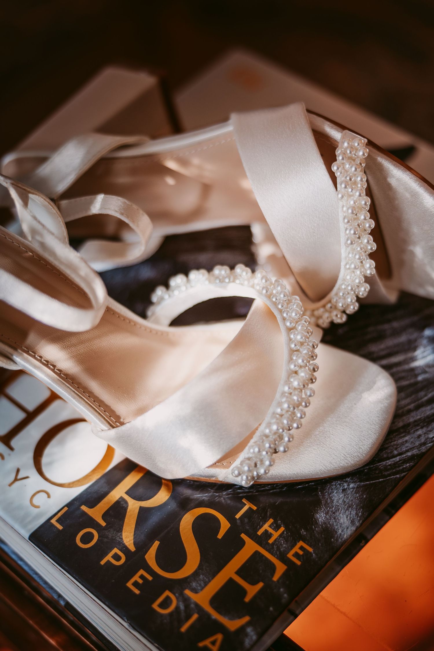 Ivory block-heel wedding sandals with pearl-trimmed straps rest on top of a horse magazine before the ceremony.