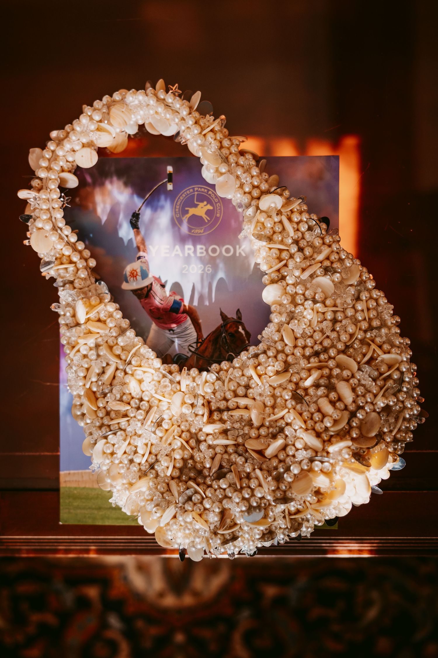 Handmade pearl and shell decorated frame around a yearbook-style horse racing poster displayed at a wedding.
