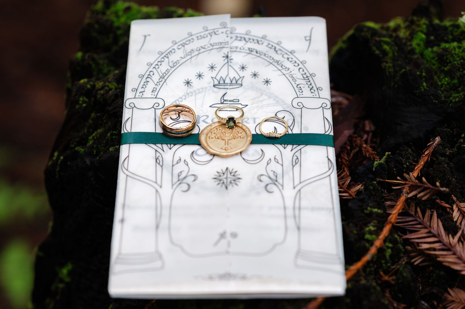 Moss-covered tree stump styled with a fantasy sword, white bridal shoes, wedding invitations, books, and floral accents in a forest setting.