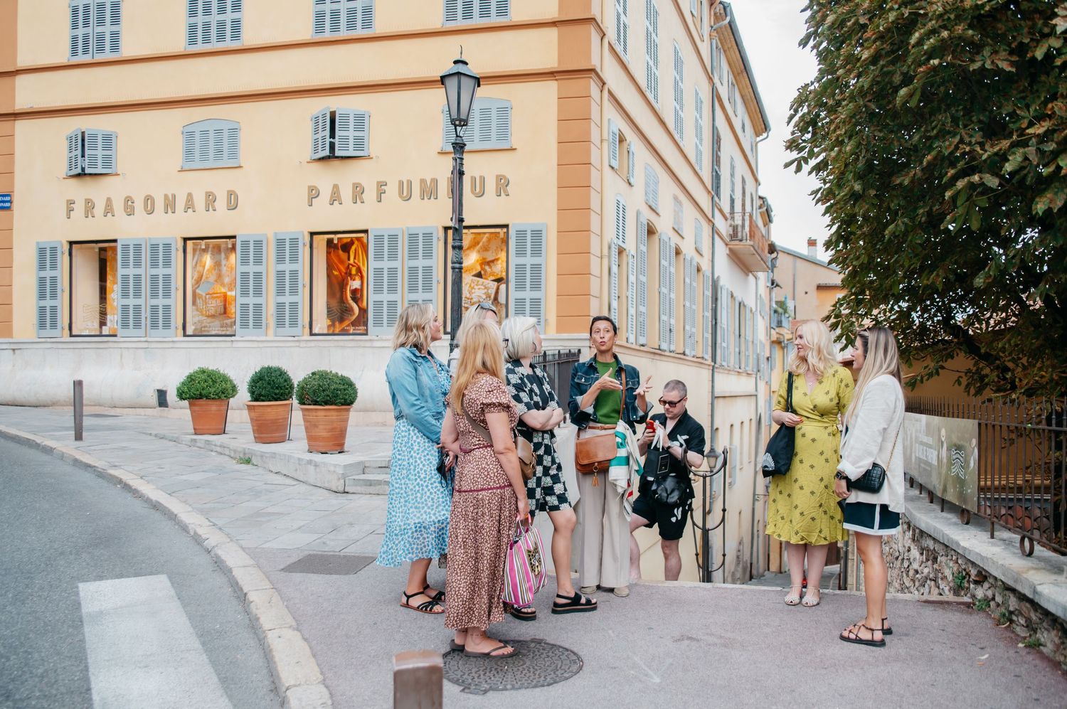 Group of tourists gathered outside Fragonard Parfumeur store on a charming street in Grasse, France.