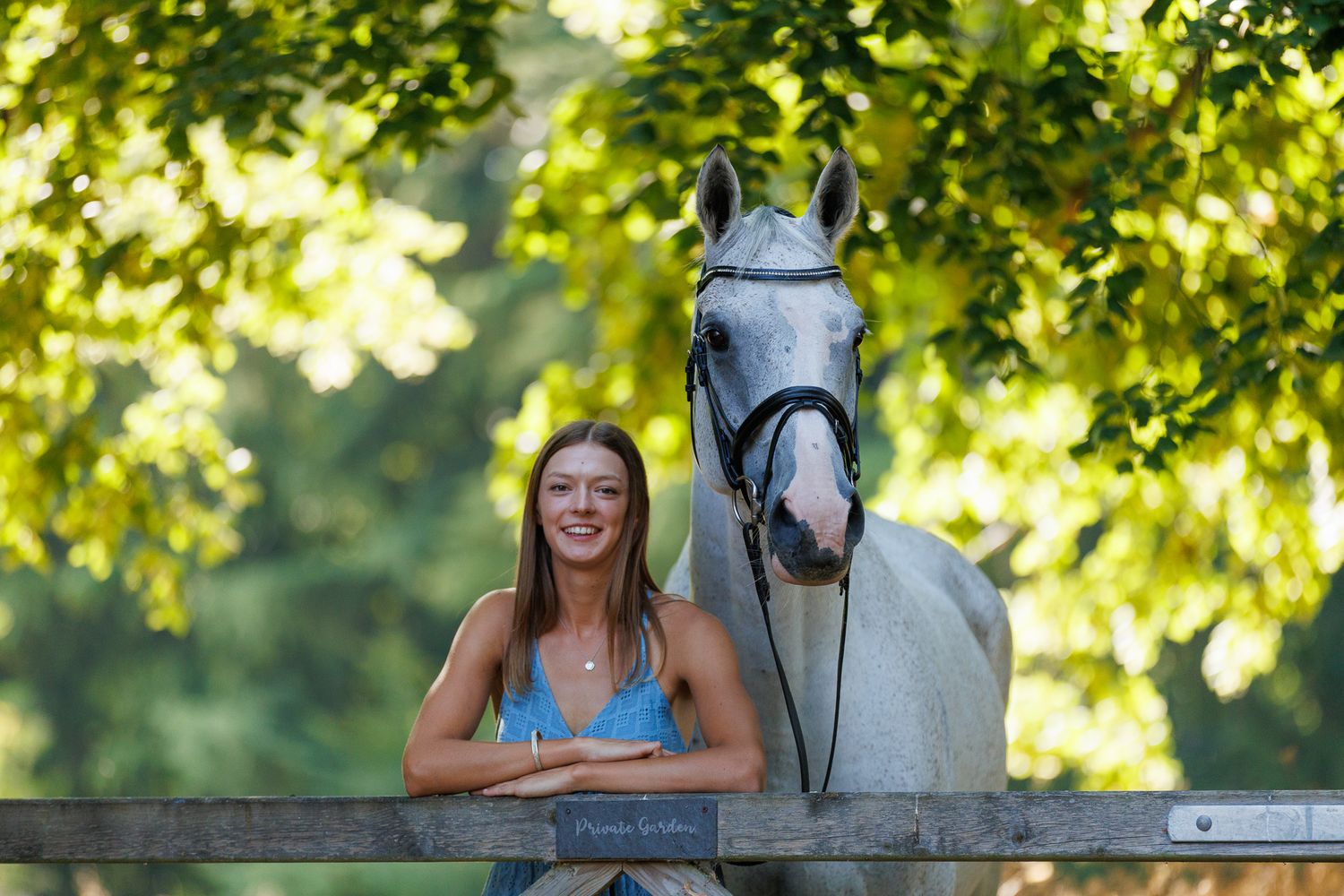Two riders stand with their animals - a dog and a dark horse relaxing outdoors in a black and white photo.