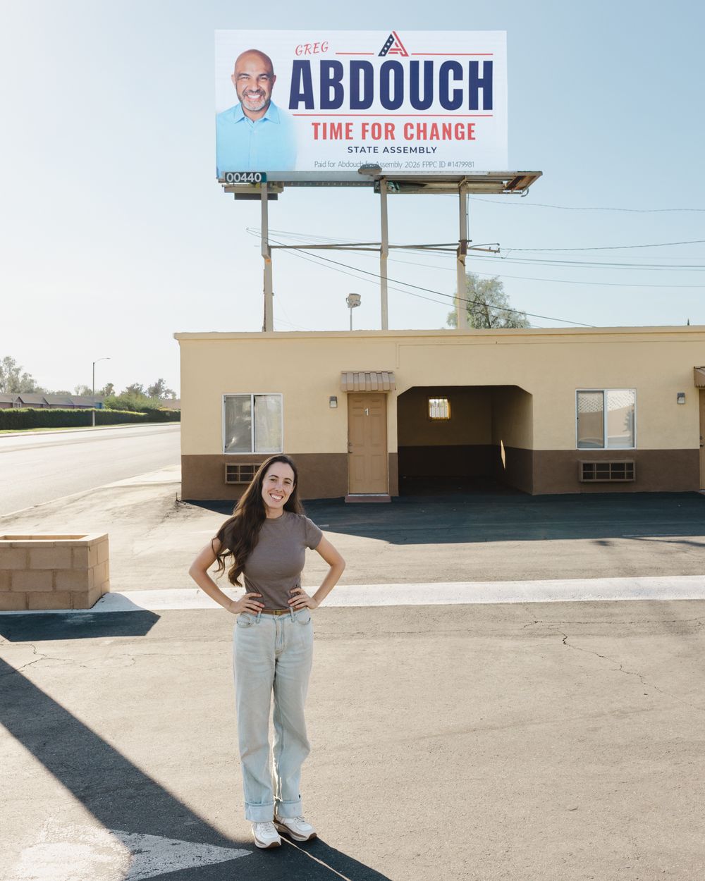 Gabrielle Johnson stands with hands on hips in a parking lot beneath a large Abdouch State Assembly Time for Change billboard.