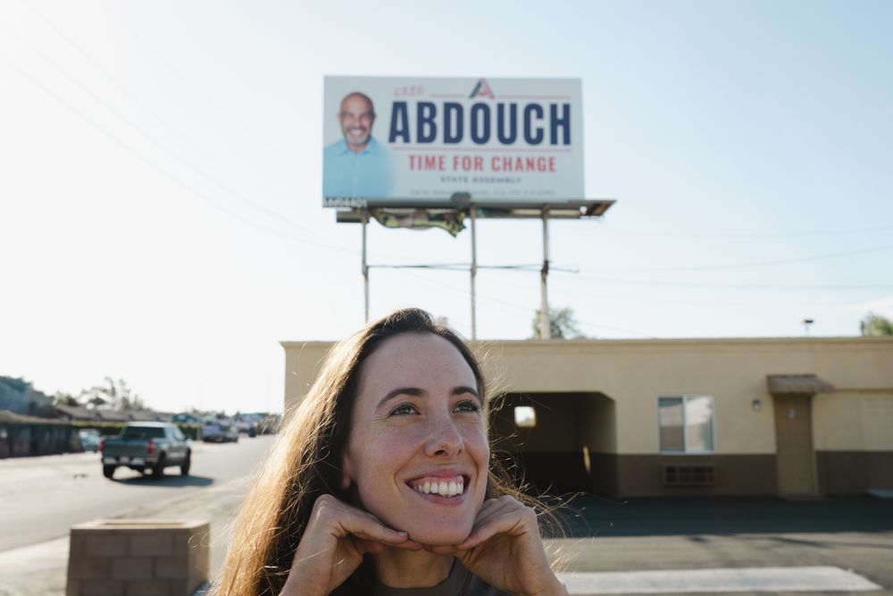 Gabrielle Johnson poses with hands under her chin in front of a roadside billboard reading Abdouch Time for Change.