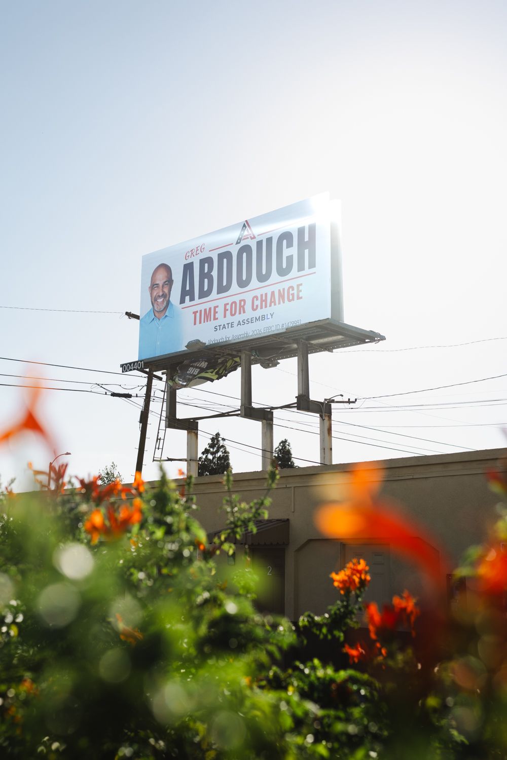 Billboard reading Abdouch, Time for Change, State Assembly, above a wall with bright orange flowers in the foreground.