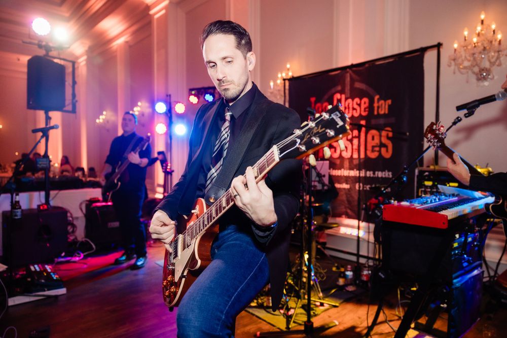 Guitar player performs on stage with band at evening event with red and blue lighting effects.