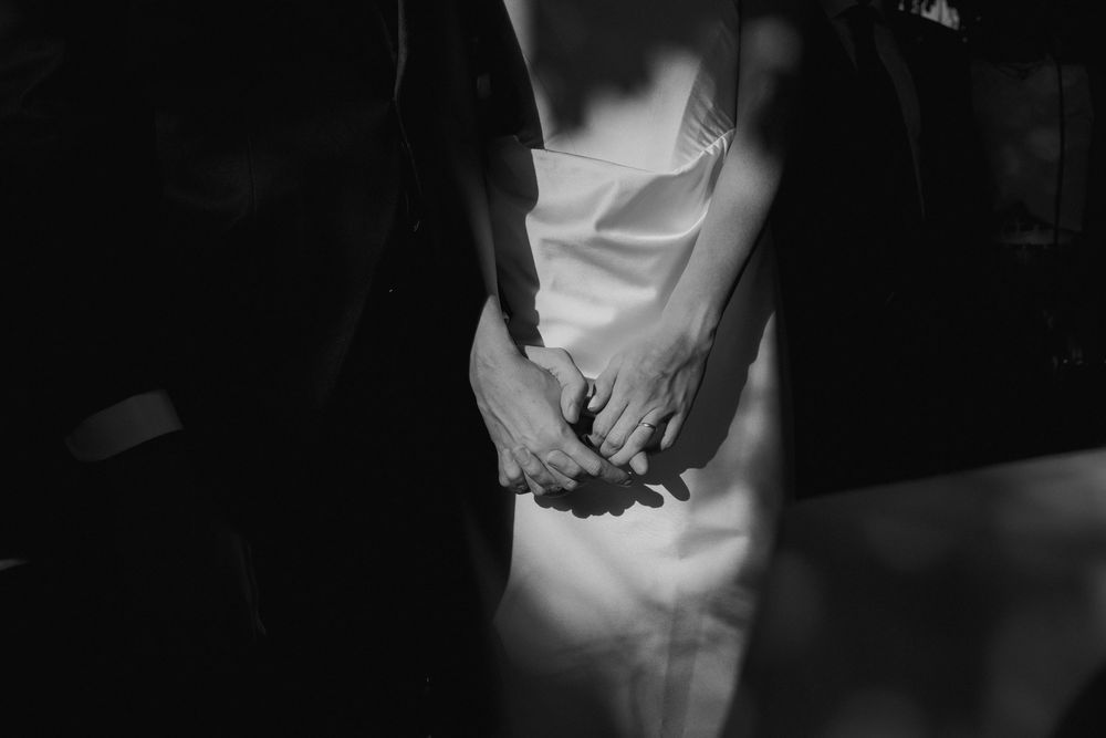 Black and white close-up of a bride and groom holding hands, with soft light highlighting the bride's white dress.