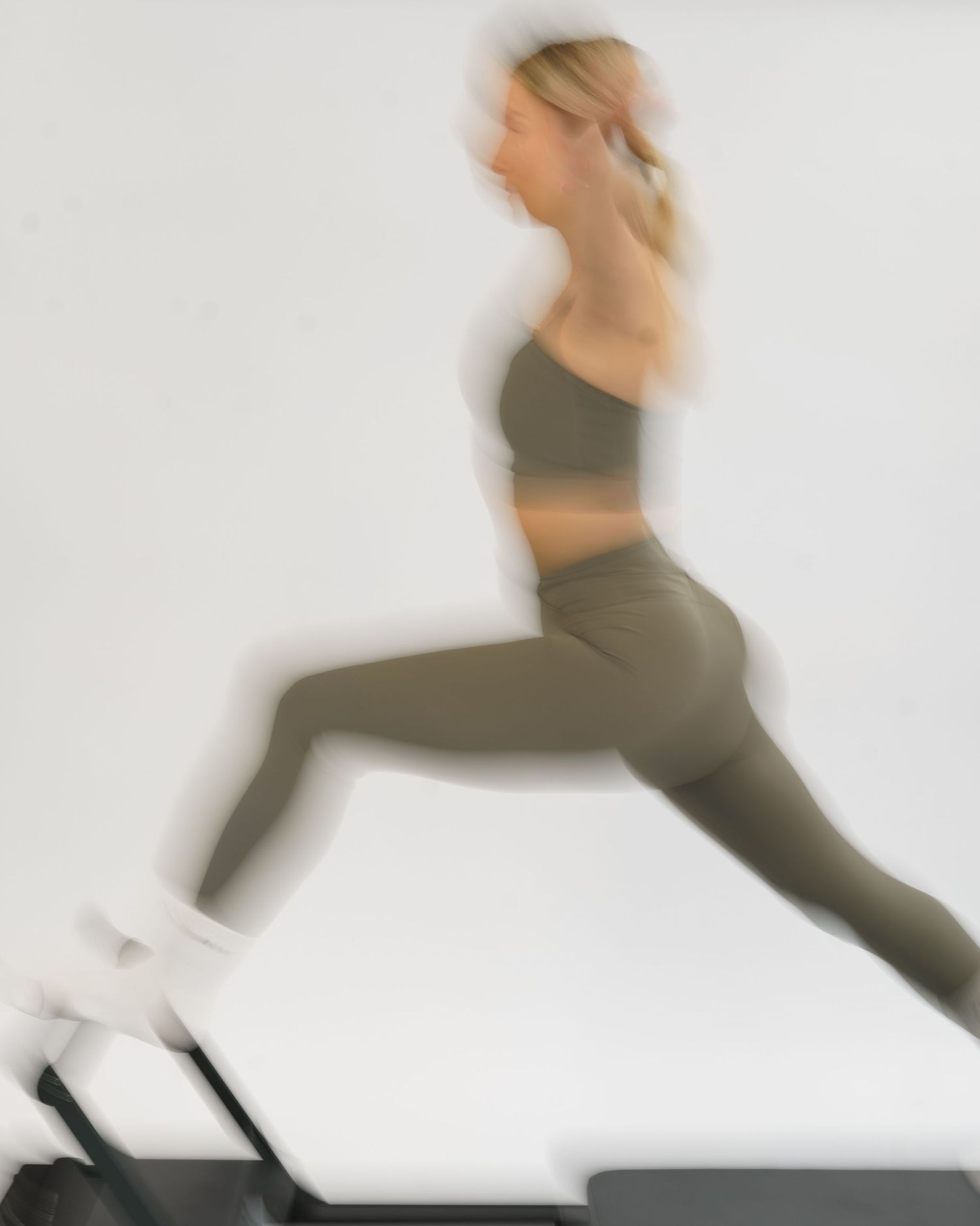 Woman in olive green sports bra and leggings running on a treadmill, captured in motion blur.