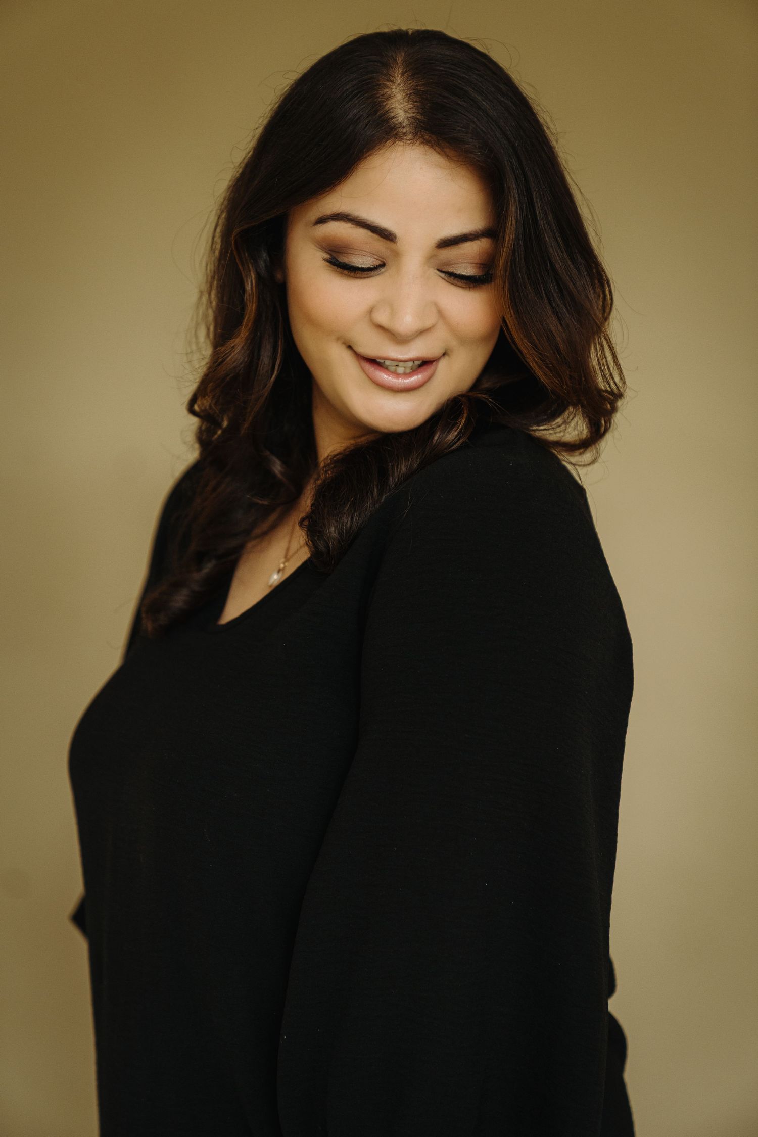A young woman with dark hair smiles softly, wearing a black blazer against a warm beige background.