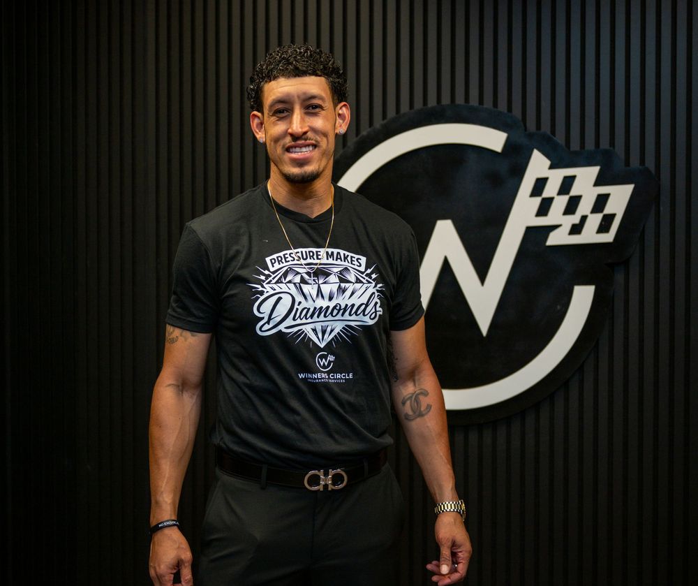 Athletic man smiling in black Diamonds graphic t-shirt, standing confidently in front of a dark branded wall.
