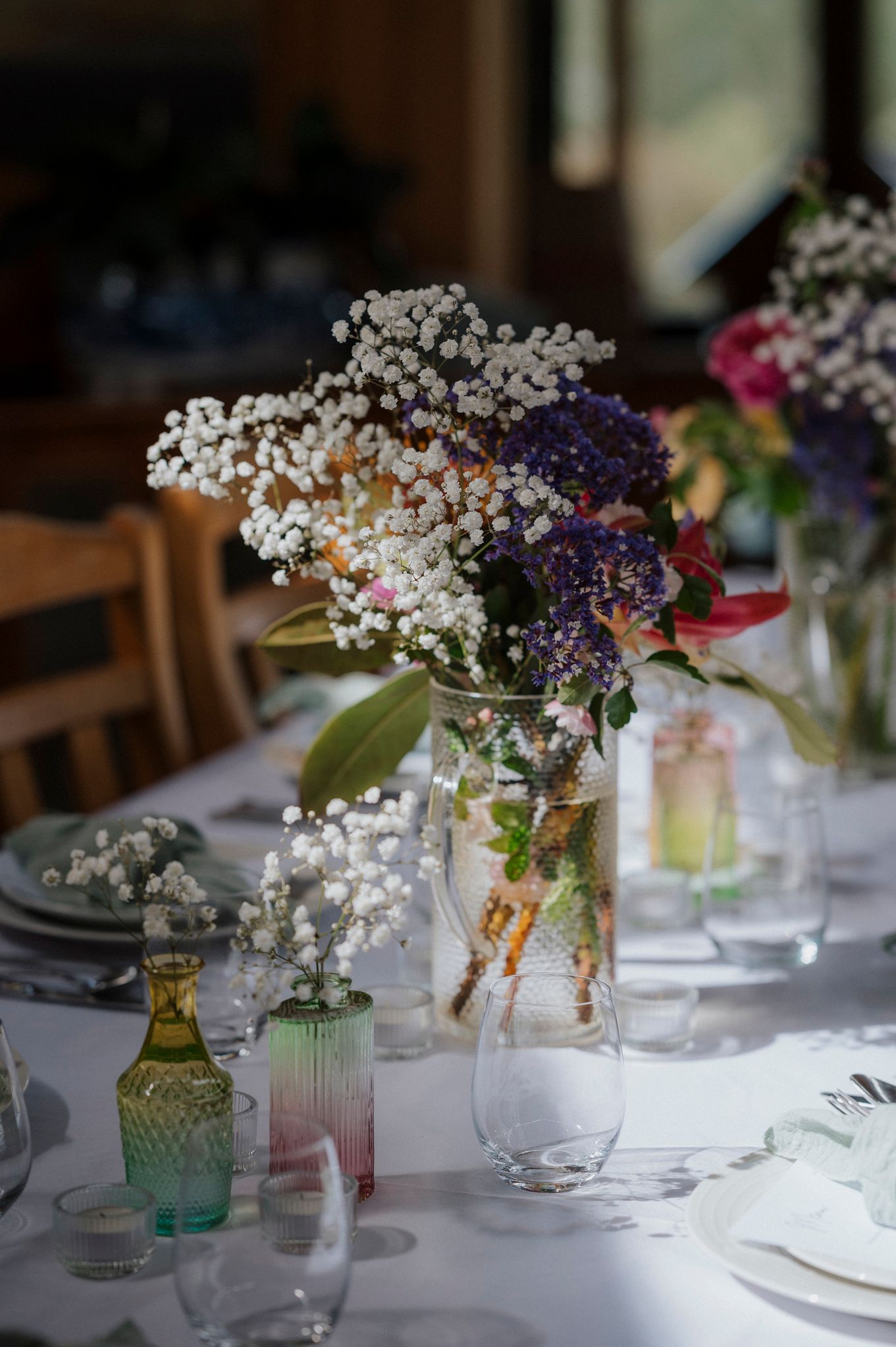 Elegant wedding table centerpiece with baby's breath and colorful flowers in glass vases on a white tablecloth.