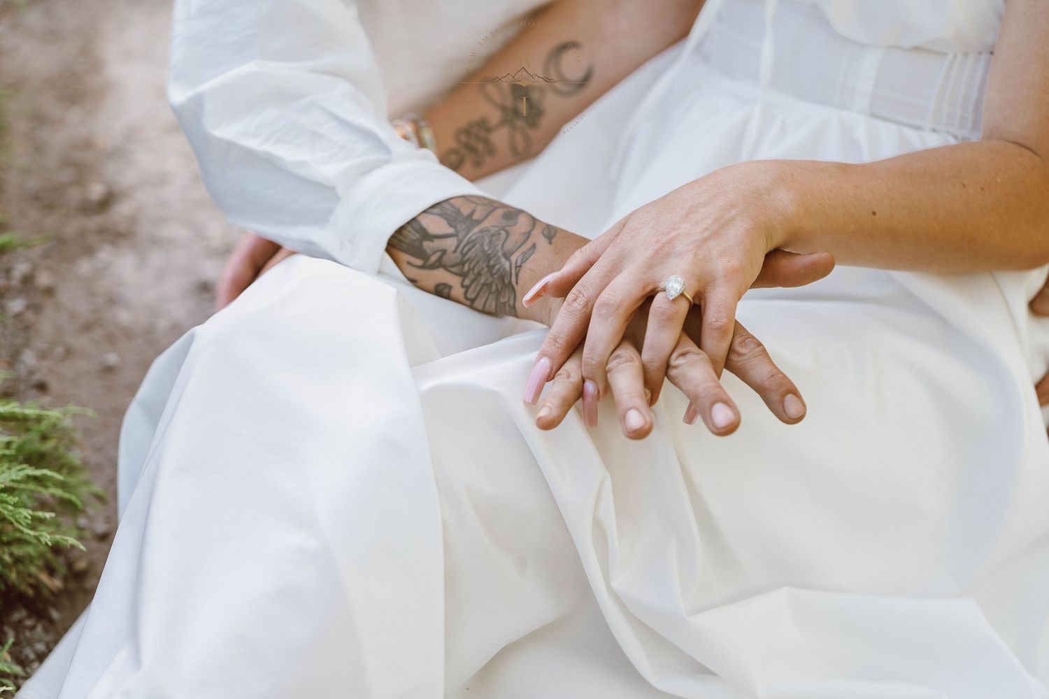 Close-up of a couple's hands with wedding rings, bride in white dress, groom with tattoos.