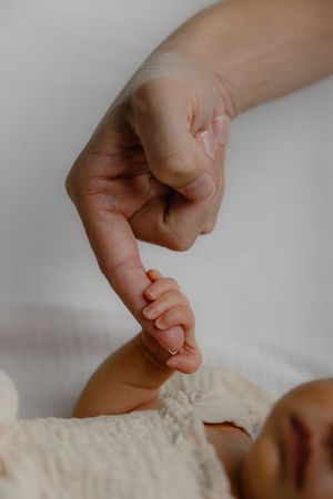 A newborn baby grasping an adult's finger, showcasing the tiny hand and precious bond between parent and child.