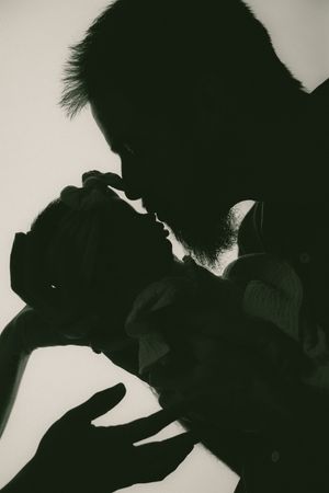 Silhouette of a father tenderly kissing his newborn baby in a black and white portrait photo.