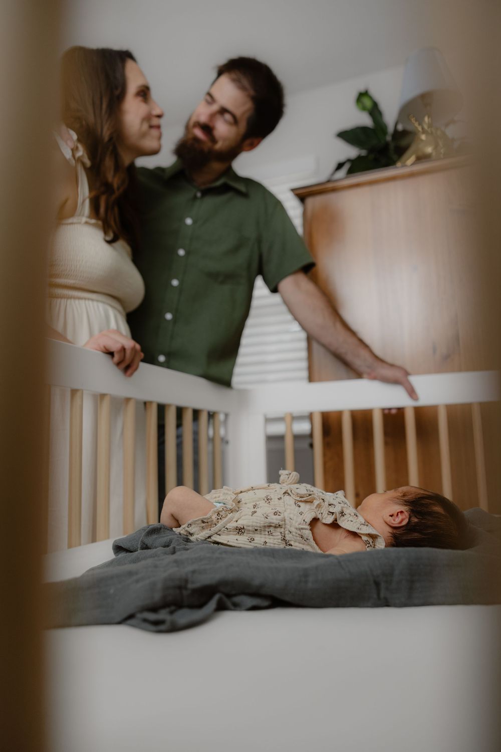 Parents share a tender moment over their newborn baby sleeping peacefully in a wooden crib.