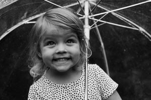 Cheerful young girl smiling under a clear umbrella in a black and white close-up portrait.