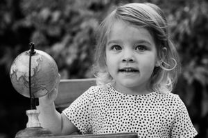 Black and white photo of a toddler girl holding a small globe, looking curious outdoors.