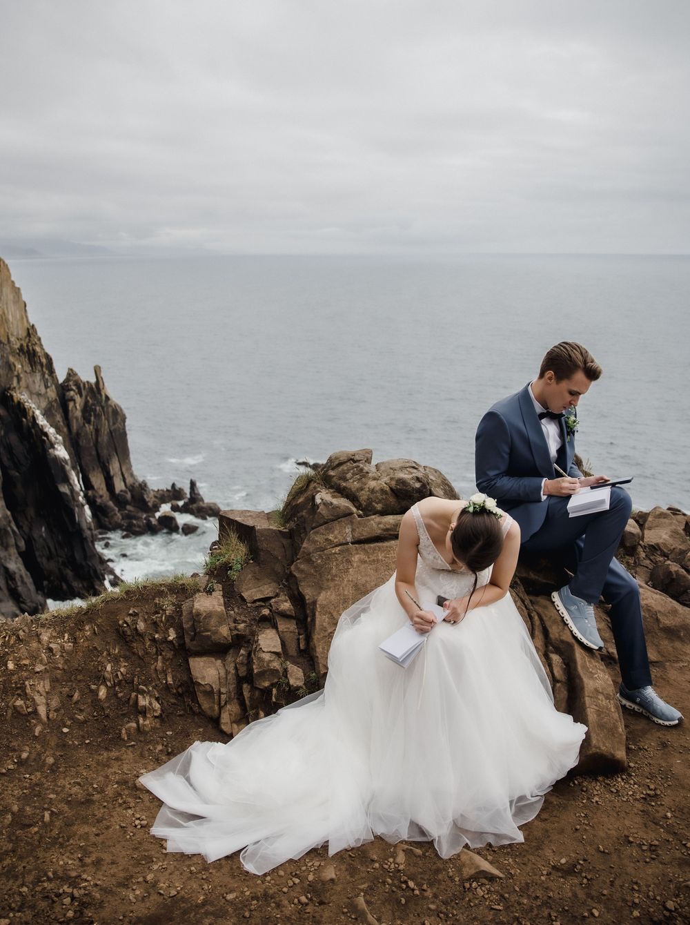 Bride and groom reading vows on rocky coastal cliffs overlooking the ocean on their wedding day.