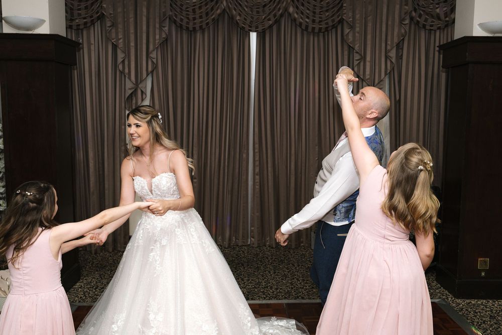 Bride and groom dancing with young flower girls in pink dresses at elegant wedding reception venue.