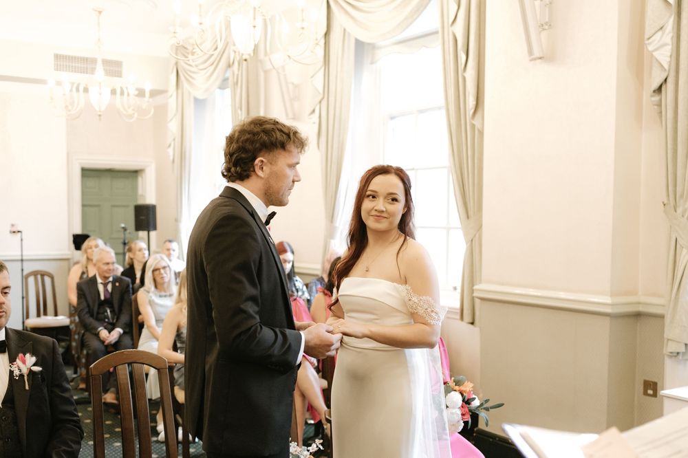 Bride and groom exchanging vows during an elegant indoor wedding ceremony in a grand white room.