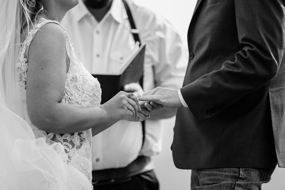 Black and white photo of a bride and groom exchanging rings during a wedding ceremony with an officiant.