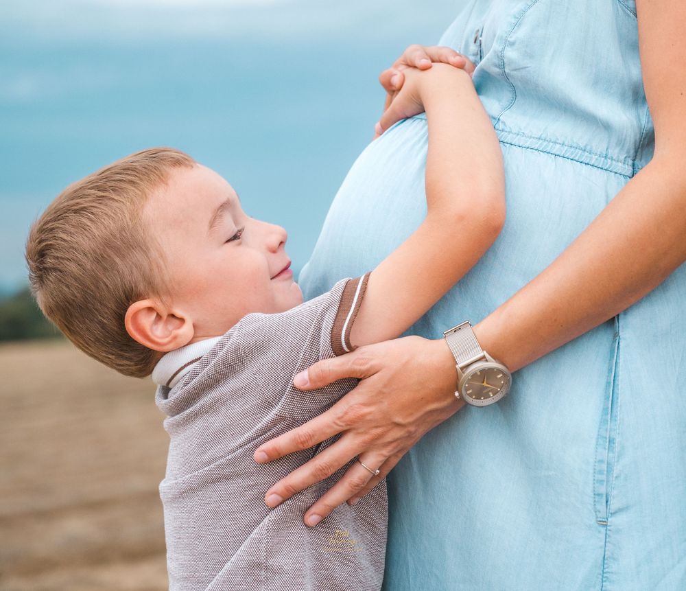 Jeune garçon posant tendrement la main sur un ventre de femme enceinte (robe bleue)