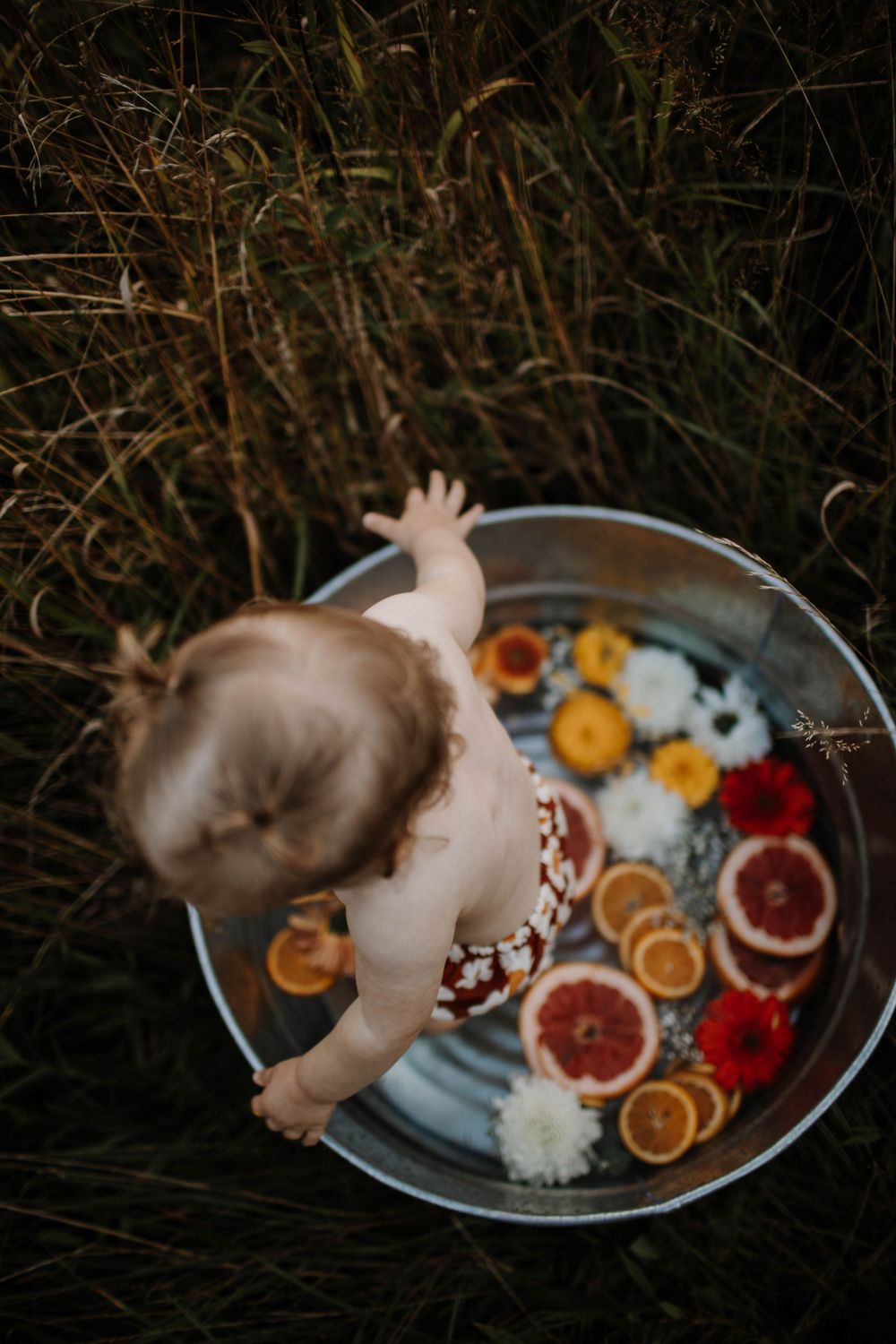 Overhead view of a baby sitting in a metal tub filled with citrus slices and flowers.