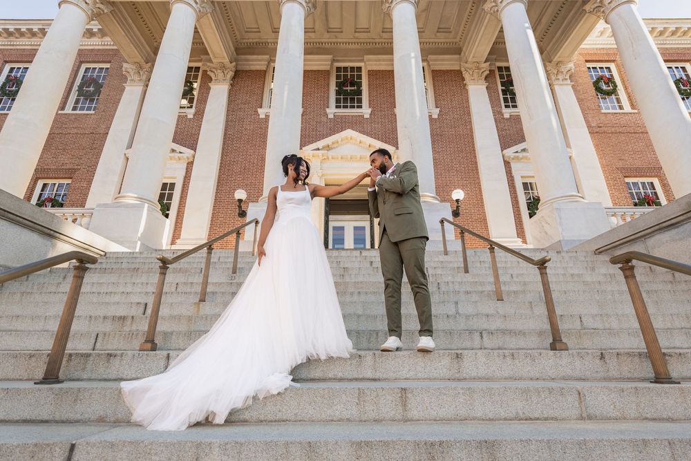 Bride and groom pose on grand steps of brick building with white columns during outdoor wedding ceremony.