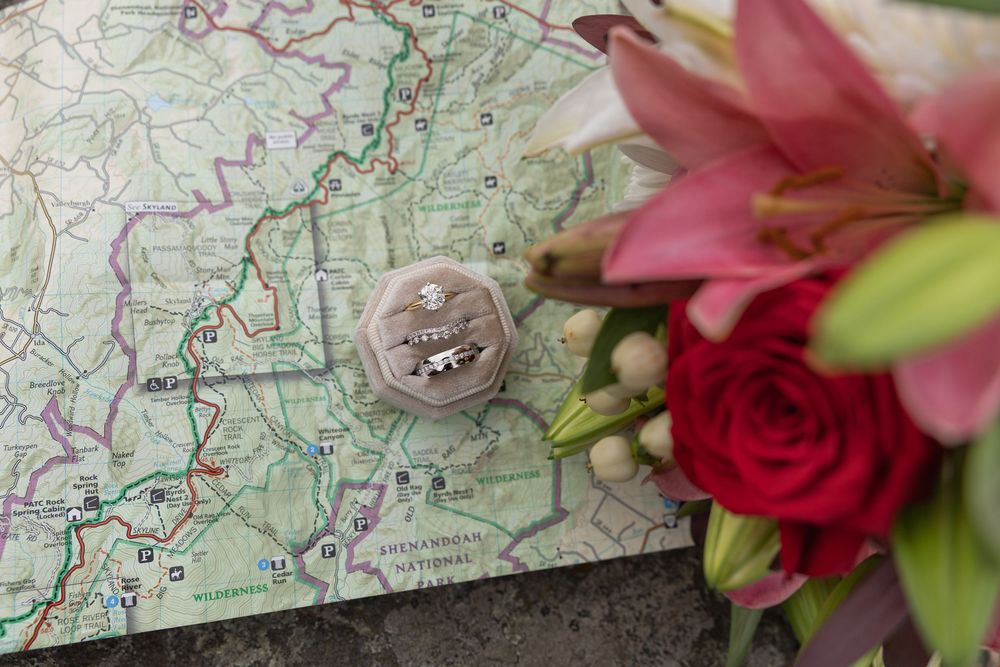 Wedding rings in a velvet box on a map, beside a bouquet of pink lilies and red roses.