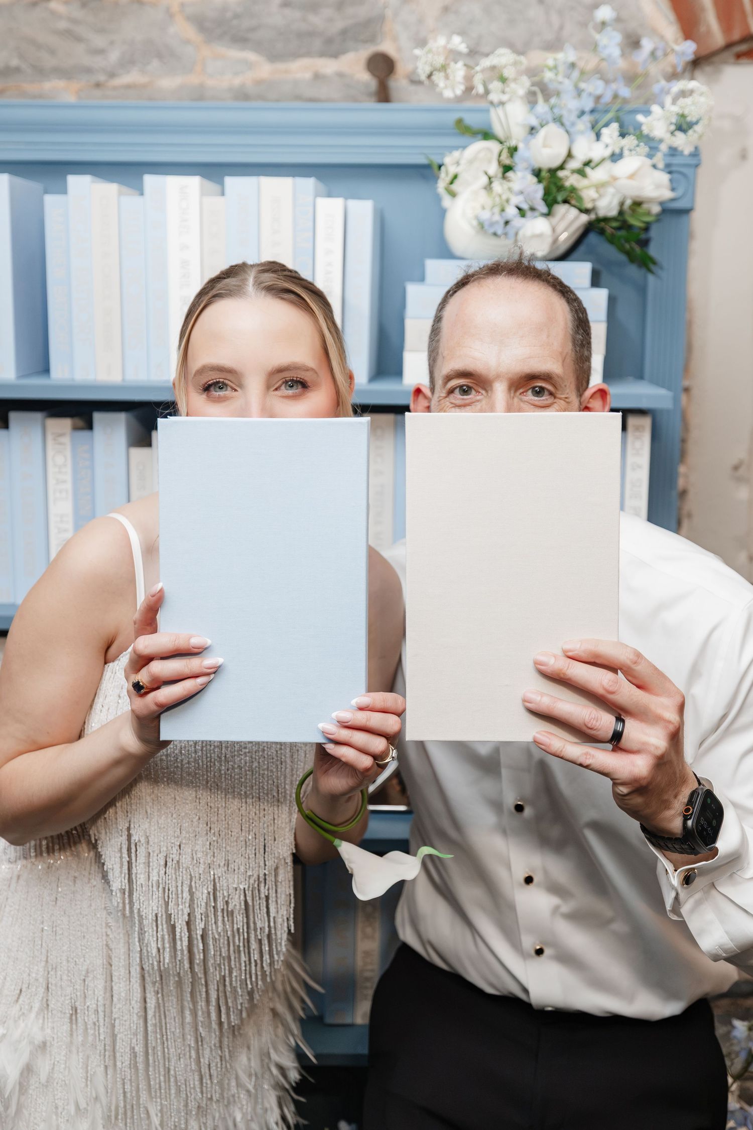 Bride and groom playfully hide faces behind blue and cream menus at wedding reception decor display.