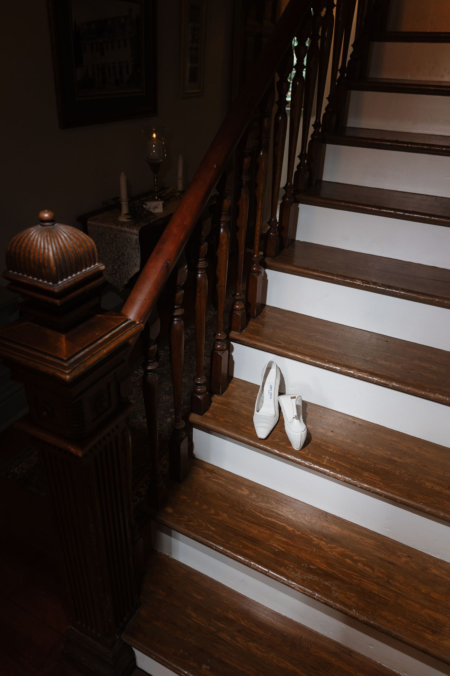 Jimmy choo bridal heels rest on a dark wooden staircase with candlelit newel post in a classic home.