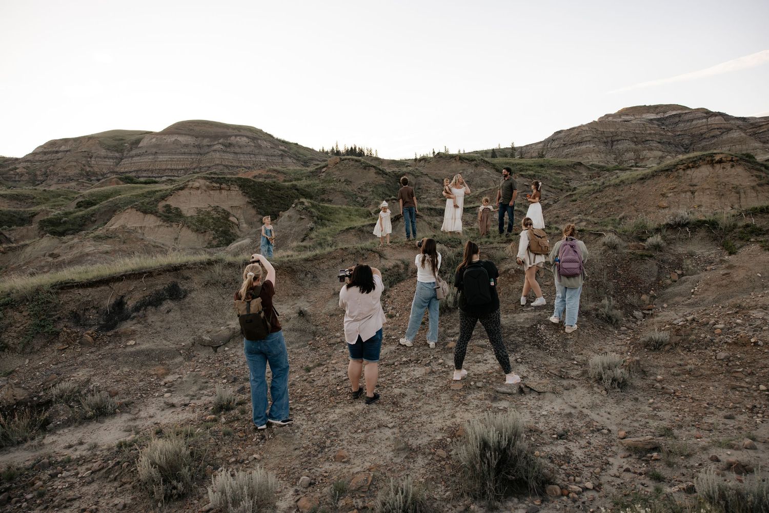 Group of people exploring rugged badlands terrain with rolling hills and vast open sky at dusk.
